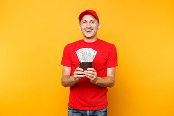 Wall Mural - Delivery man in red uniform isolated on yellow orange background. Professional male employee in cap, t-shirt courier or dealer holding bundle lots of dollars, cash money. Service concept. Copy space.