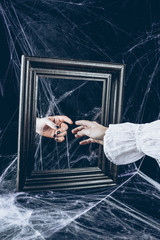 cropped view of woman touching to reflection in mirror with scary spider web around