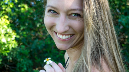 Cute portrait of young blonde woman face smoking daisy flower weed smiling laughing with blue eyes isolated in nature