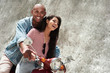 © Friends Stock - Romantic Relationship. Young diverse couple riding bike on the city street together smiling happy