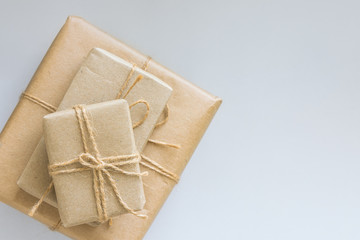 Stacked gift boxes wrapped in brown craft paper tied with twine various sizes. White background top view. Christmas New Years corporate family presents shopping concept. Copy space