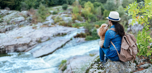 Wall Mural - Woman traveler with backpack holding dog and looking at natural canyon with view of the mountain river.