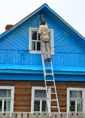 Wall Mural - The man makes up a facade of the wooden house, standing on a ladder