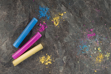 Blue, magenta and yellow pastel crayons and spots of pigment dust on dark textured stone background of granite. Copy space. Selective focus