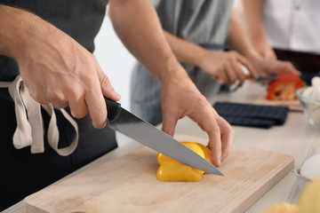 Wall Mural - Male chef cutting paprika on wooden board at table, closeup