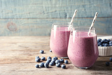 Tasty Blueberry Smoothie In Glasses And Berries On Wooden Table Against Color Background With Space For Text