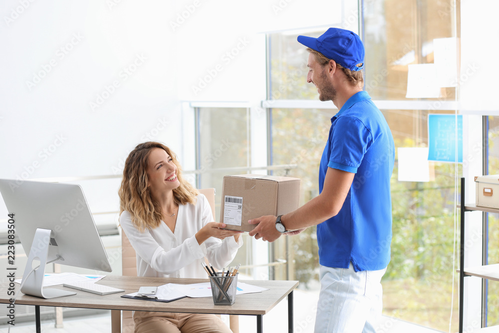 Young woman receiving parcel from courier in office - obrazy, fototapety, plakaty 