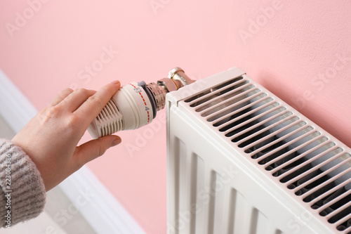 Fotografía Woman adjusting heating radiator near color wall