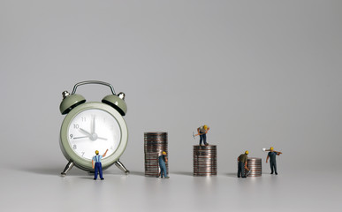 Miniature working person with piles of coins in front of the alarm clock.