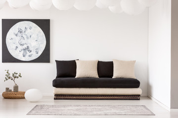 Poster - Pillows on black sofa near carpet in white living room interior with plant and moon poster. Real photo