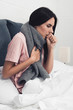sick young woman sitting in bed and having cough