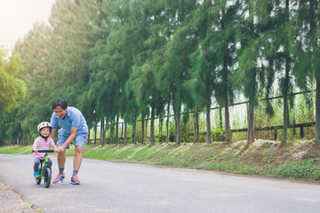 Young father spend time with Cute little Asian 2 years old toddler boy child, Dad and son having fun with balance bike (run bike) on nature, Dad tech son to ride bike, father's day concept - film look