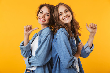 Poster - Women friends posing isolated over yellow background pointing.