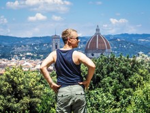 A Blond Man In Sunglasses Posing Back To The Camera On The Background Of A Panoramic View Of The City Of Florence, The Roof And The Cathedral Of Boboli Park