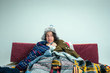 © master1305 - The young sick woman with flue sitting on sofa at home or studio covered with knitted warm clothes. Illness, influenza, pain concept. Relaxation at Home. Healthcare Concepts.