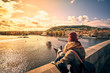 Young women tourist with a puppy dog and a backpack looking at the tourist boat and swans sailing on Vltava river from the Charles Bridge (Karluv Most) in Prague, Czech Republic