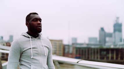 Poster - A close up of young sporty black man walking on the bridge in a city.