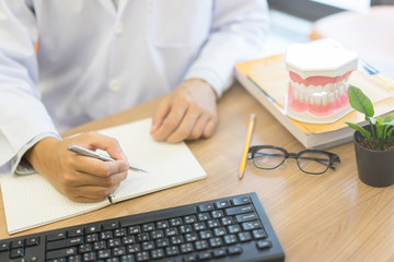 close up dentist hand writing on notebook after finished diagnose about teeth symptom at clinic office concept