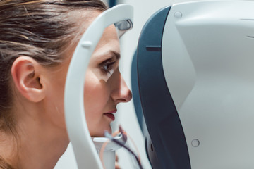 Woman having eyesight test using modern refractometer looking into the machine 