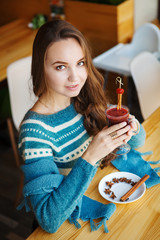 Brown-haired woman drinking smoothie with cinnamon alone in cafe