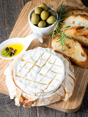 Wall Mural - Baked camembert cheese. Fresh Brie cheese and a slice on a wooden board with nuts, honey, rosemary, baguette bread grilled toasts and leaves. Brie type of cheese. Italian, French cheese.