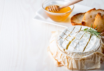 Baked camembert cheese. Fresh Brie cheese and a slice on a wooden board with nuts, honey, rosemary, baguette bread grilled toasts and leaves. Brie type of cheese. Italian, French cheese.