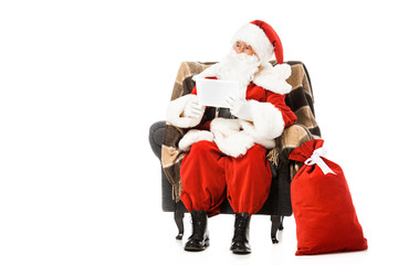 santa claus sitting in armchair with tablet and looking away isolated on white