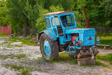 The Old Blue Tractor Without Front Wheels In The Russian Village