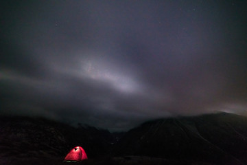 Wall Mural - illuminated tent by night on the alps with clouds and fog. camping under starry sky, summer adventur