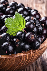 Wall Mural - Big wooden bowl with fresh black currant and original leave on wooden background close-up.