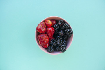 Canvas Print - Flat lay of freshly picked various berries in a bowl on blue background.