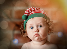 Little Baby Boy In Elf Hat With Christmas Fairy Lights On Background. Christmas Time Season Image