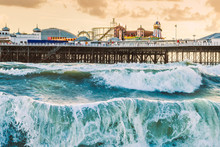 Brighton Pier, Brighton, Sussex, Britain On A Storm Evening At Dusk As The Sun Is Setting. There Are High Waves And Surf On The Beach
