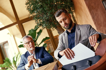 Wall Mural - Business lunch. Two business people in the restaurant sitting at table one man taking contract from case serious. Team work concept