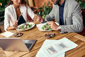 Wall Mural - Business lunch. Man and woman sitting at table at restaurant eating healthy fresh salad discussing project close-up