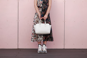 Woman in a fashionable dress with a white stylish bag stand near the pink wall. Women's Fashion Sneakers