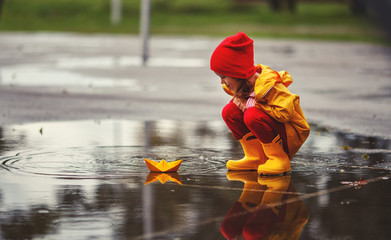 Wall Mural - happy child girl with umbrella and paper boat in   puddle in   autumn on nature.