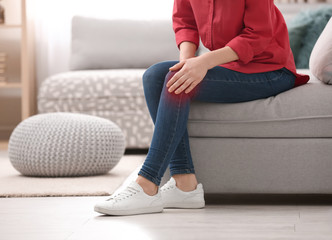 Wall Mural - Young woman suffering from knee pain at home