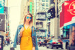 Young Eastern European Woman traveling in New York, with long brown hair, wearing yellow dress, blue Denim jacket draped over shoulder, blue sunglasses, walking on street in Times Square of Manhattan