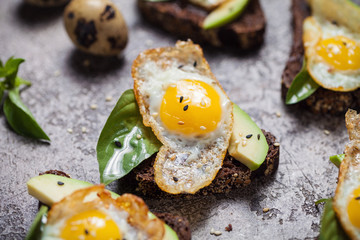 toast brown bread with quail egg and avocado, basil on table