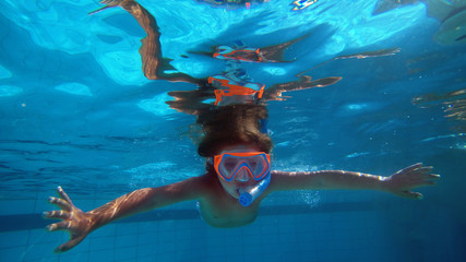Portrait of a little girl (kid) while she is swimming in a swimming pool with the mask and te