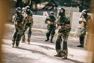 paintball team in uniform and protective masks playing paintball with marker guns outdoors