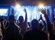 © Dickov - Crowd with raised hands in front of stage with colorful lights.