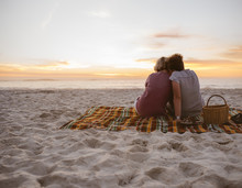 Young Lesbian Couple Sitting On Beach Blanket Watching The Sunset
