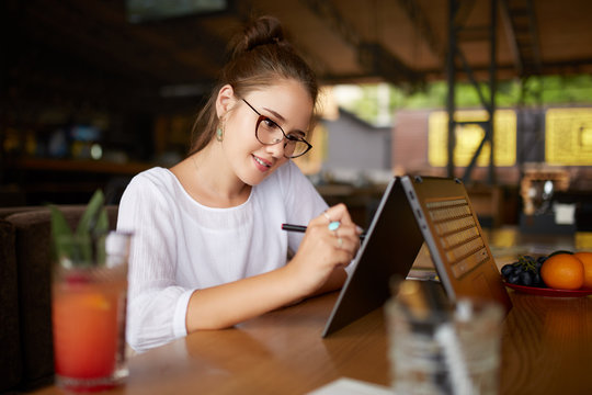 Digital artist drawing sketch with stylus on convertible 2 in 1 laptop display in tent mode. Mixed race multiethnic asian caucasian woman working on project design or writing notes on touchscreen.