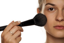 Young woman applying powder foundation with brush on white background