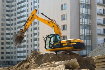 Yellow construction excavator near a multi-storey building under construction.