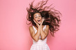© Drobot Dean - Photo of beautiful woman 20s wearing dress smiling and shaking her long brown hair, isolated over pink background