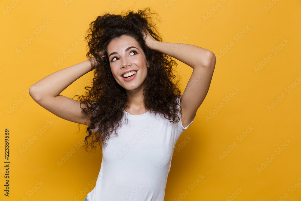 Image of young european woman 20s with curly hair smiling and grabbing head, isolated over yellow background - obrazy, fototapety, plakaty 