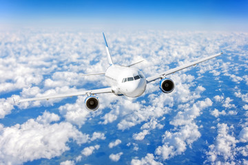 Commercial airplane flying over bright blue sky and white clouds.